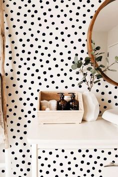 a white dresser topped with a mirror next to a wall covered in black polka dots