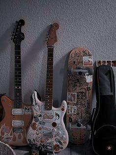 three guitars are lined up against the wall, one has a guitar case on it