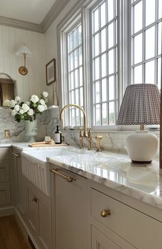 a white kitchen with marble counter tops and gold faucets on the windowsill