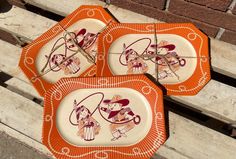 three orange plates sitting on top of a wooden bench next to a brick wall, with cartoon characters painted on them