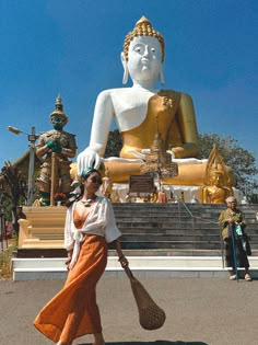 a woman is walking in front of a large buddha statue