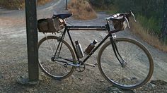 a bicycle parked next to a sign on a dirt road with grass and trees in the background