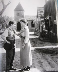 an old black and white photo of two women standing next to each other in front of a house