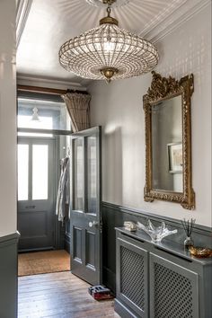 an ornate chandelier hangs from the ceiling in this entryway with gray painted walls and wood flooring