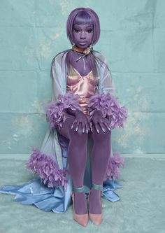 a doll with purple hair sitting on top of a blue sheeted floor next to a wall