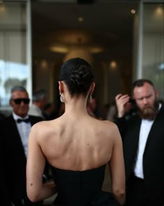 the back of a woman in a black dress at an event with other people behind her