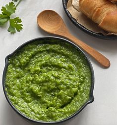 a bowl of guacamole next to a wooden spoon on a white surface