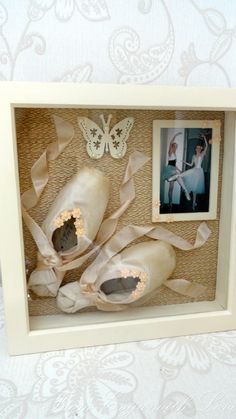 a shadow box with ballet shoes in it and a butterfly on the wall next to it