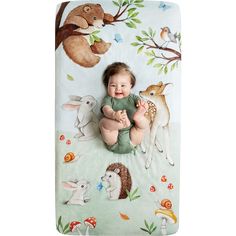 a baby laying on top of a blanket in front of a forest scene with animals