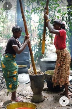 two women are standing in front of pots and holding wooden poles with numbers on them