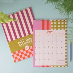 two calendars are sitting on a desk next to a pencil and plant with leaves