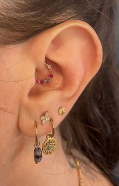 a close up of a person's ear with different colored stones on it and gold hoops