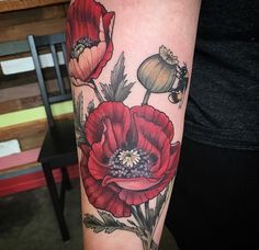 a woman's arm with red flowers on it and a bee flying in the air