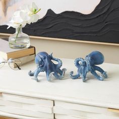 two blue octopus figurines sitting on top of a white table next to a book