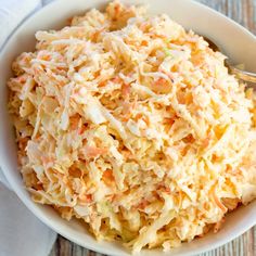 a white bowl filled with coleslaw sitting on top of a wooden table next to a fork