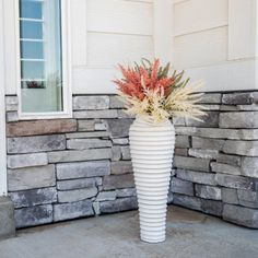 a tall white vase with flowers in it on the front porch next to a stone wall