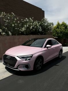 a pink car is parked on the side of the road near some bushes and flowers