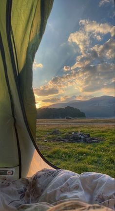 the sun is setting over an open field with a tent and mountains in the background