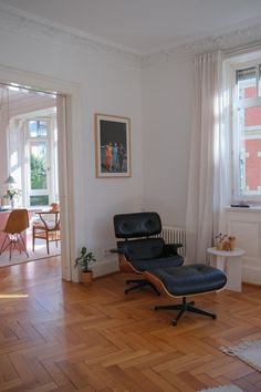 a living room with hard wood floors and an eames chair in front of a window