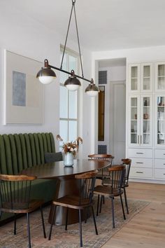 a dining room table with chairs and lights hanging from it's ceiling, in front of a built - in bookcase