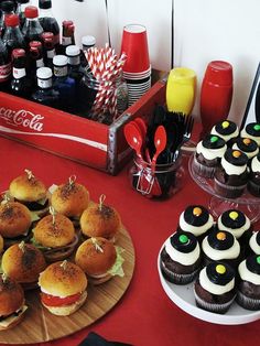 a table topped with cupcakes covered in frosting next to bottles of soda