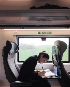 a woman writing on a paper while sitting in a seat next to an open window