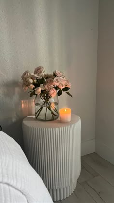 a vase filled with flowers sitting on top of a white table next to a bed