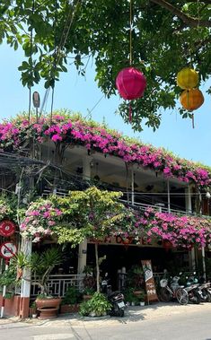 several colorful umbrellas hanging from the side of a building with flowers growing on it