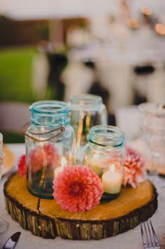 mason jars filled with flowers and candles sit on a wooden slice at the center of a table