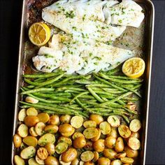 fish, potatoes and asparagus in a pan with lemons on the side