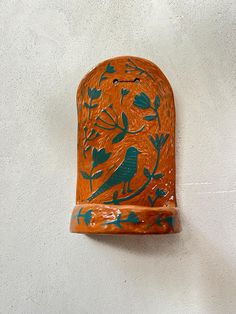 an orange vase with blue birds and flowers painted on it's side against a white wall