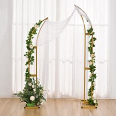 an arch decorated with flowers and greenery in front of a white drape curtain