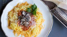 a white plate topped with spaghetti and mushrooms next to a grater on top of a table