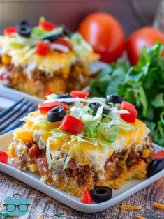 two plates filled with taco casserole on top of a table next to vegetables