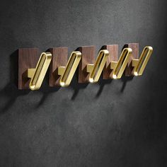 three brass and wood hooks hang on a black wall