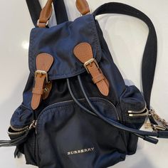 This Is An Authentic Burberry Nylon Medium Rucksack Backpack In Black. This Chic Backpack Is Crafted Of Nylon Canvas In Black With Tan Calfskin Trims. The Bag Features Adjustable Shoulder Straps, A Front Pocket, Two Side Pockets, And Polished Gold Hardware. The Top Opens To A Black Burberry Fabric Interior With A Zipper And Patch Pocket. Excellent Condition. Approx Measurement: Base Length: 8.25 In Height: 12.5 In Width: 5.5 In Drop: 3 In Drop: 12 In Burberry Rucksack, Chic Backpack, Rucksack Backpack, Black Backpack, Burberry Bag, Gold Hardware, Patch Pocket, Front Pocket, Calf Skin