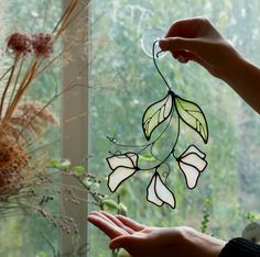 a hand holding a stained glass piece with leaves on it and flowers in the background