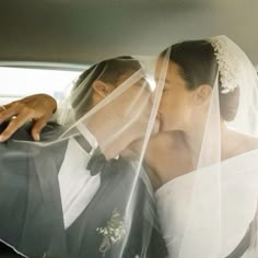 a bride and groom kissing in the back seat of a car with veils over their heads