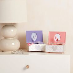 two small boxes sitting on top of a white dresser next to a lamp and vase