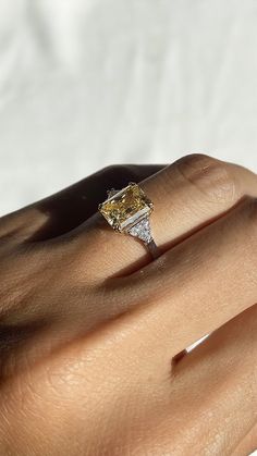 a woman's hand holding an engagement ring with a yellow diamond in the center