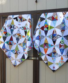 two quilts are hanging on the side of a building, one has been made to look like hexagonal kites