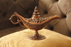 an ornate metal teapot sitting on top of a yellow velvet cushion in front of a couch