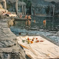 some people are swimming in the water and one person is laying on a towel with fruit