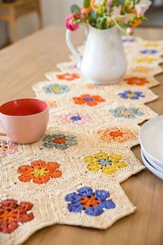 crocheted placemats on a wooden table with plates and flowers in the vase