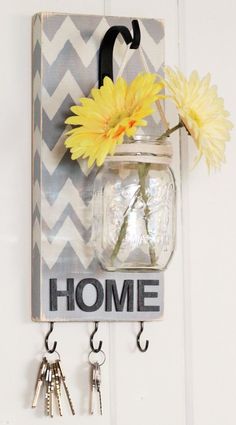 a mason jar hanging on a wall with key hooks and a yellow flower in it