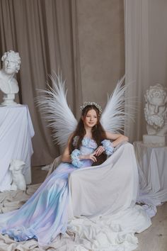 a woman sitting on top of a bed wearing a white dress and angel wings over her head