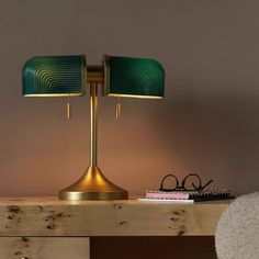 a green lamp sitting on top of a wooden table next to a pair of glasses