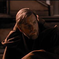 a man with long hair and a beard wearing a robe sitting on the ground in front of stairs