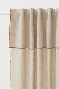 a beige curtain with orange trim hanging on a white rodo - end window sill