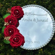 a round mirror with three red roses on it and the words aruba & junaid written in arabic